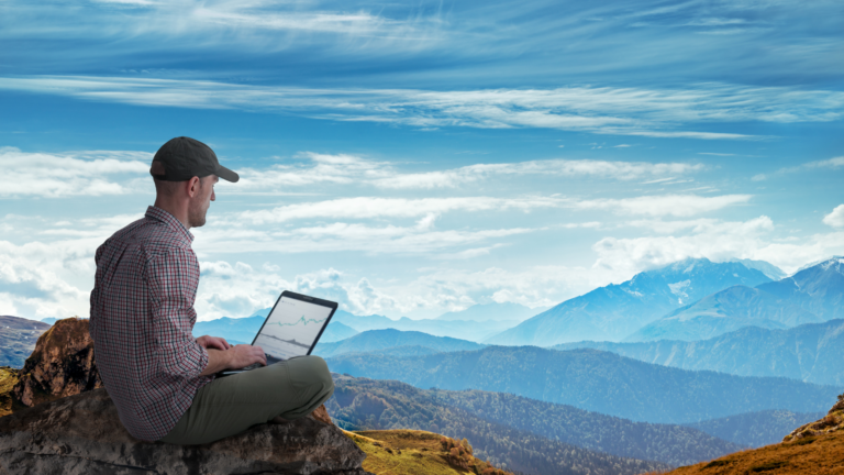 Atop a breathtaking mountain range, a man diligently focuses on his report, maintaining his remote work productivity
