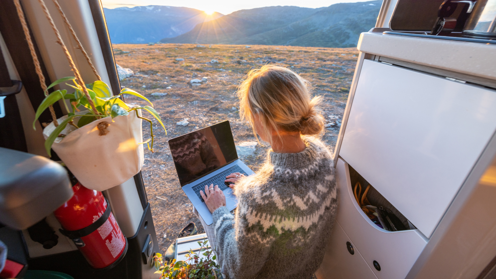 A woman enjoys working remotely out of an RV in front of a beautiful mountainscape