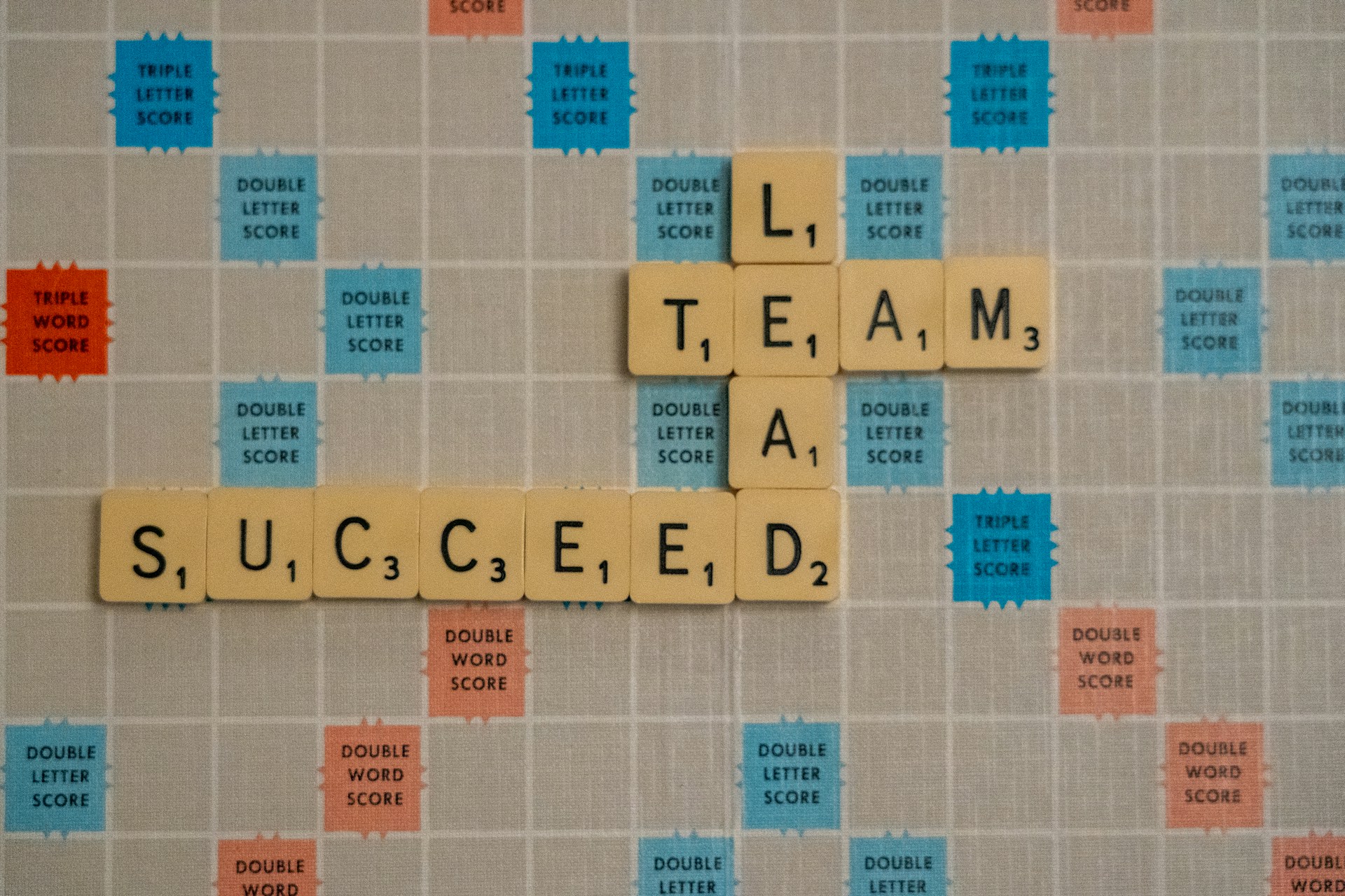 Scrabble tiles arranged on a game board to spell the words 'TEAM' and 'SUCCEED', symbolizing strategic collaboration and success in hiring and leadership.
