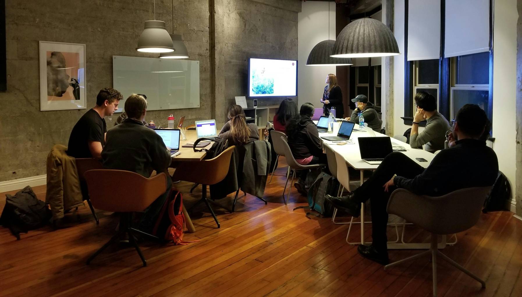 Team of professionals in a modern office gathered around a large table with laptops, listening to a woman presenting at a screen—illustrating how a Los Angeles tech startup built a leadership team that transformed its growth.