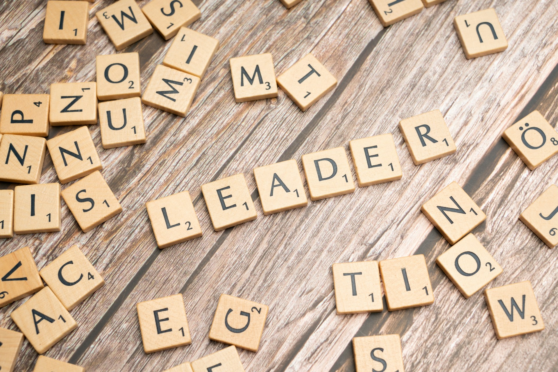 Scrabble tiles spelling the word 'Leader' surrounded by scattered letters, symbolizing the complexity of modern leadership.